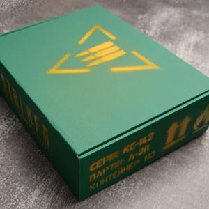 May include: A green rectangular box with a yellow triangle and arrow design on the lid. The box has text in yellow, including the word "STALKER" on the side. The box also has other text and symbols.