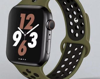 May include: A black smartwatch with a green and black perforated band. The watch face displays the time, with the numbers 12, 9, and 3 prominently visible. The band is olive green on the outside and black with white perforations on the inside.