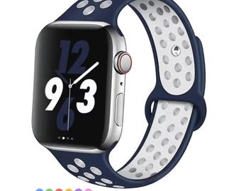 May include: A silver smartwatch with a navy blue and white perforated band. The watch face displays the time as 12:16. The band is made of a flexible material and has a contrasting white interior. The watch has a red button on the side.