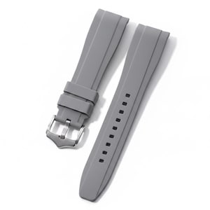 K&ouml;nnte beinhalten: Ein zweiteiliges graues Uhrenarmband aus Silikon mit glatter, matter Oberfl&auml;che, einer silberfarbenen Dornschlie&szlig;e aus Edelstahl und zwei passenden grauen Schlaufen. Das Armband verf&uuml;gt &uuml;ber eine Reihe rechteckiger Einstelll&ouml;cher.