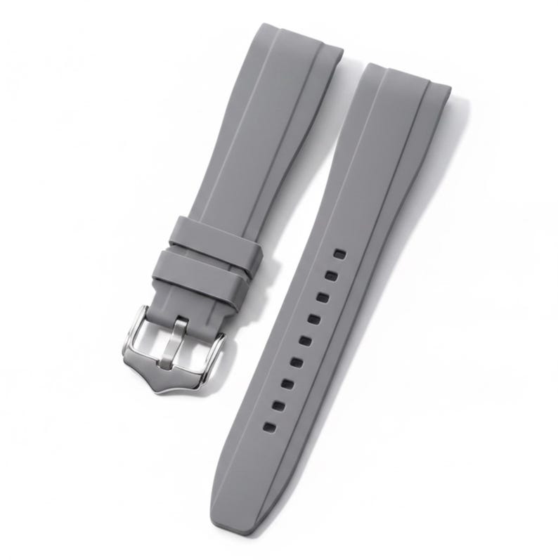 K&ouml;nnte beinhalten: Ein zweiteiliges graues Uhrenarmband aus Silikon mit glatter, matter Oberfl&auml;che, einer silberfarbenen Dornschlie&szlig;e aus Edelstahl und zwei passenden grauen Schlaufen. Das Armband verf&uuml;gt &uuml;ber eine Reihe rechteckiger Einstelll&ouml;cher.