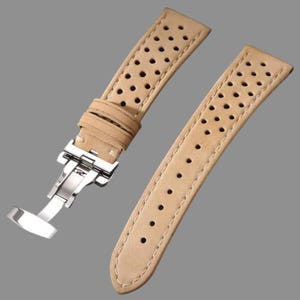 May include: Beige leather watch strap with a series of small perforations. The strap has a stainless steel clasp and is stitched around the edges. The watch band is displayed on a grey background.