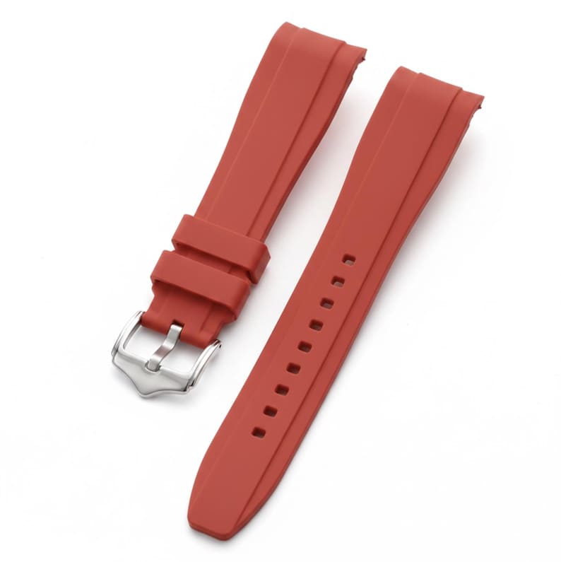 K&ouml;nnte beinhalten: Ein zweiteiliges rotes Uhrenarmband aus Kautschuk mit glatter, matter Oberfl&auml;che. Das Armband verf&uuml;gt &uuml;ber eine silberfarbene Metall-Dornschlie&szlig;e und zwei passende rote Kautschukschlaufen am k&uuml;rzeren Teil, w&auml;hrend der l&auml;ngere Teil rechteckige L&ouml;cher hat.
