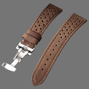 May include: Two-piece brown leather watch strap with a stainless steel clasp. The strap has a perforated design and visible stitching along the edges. The leather has a distressed appearance.
