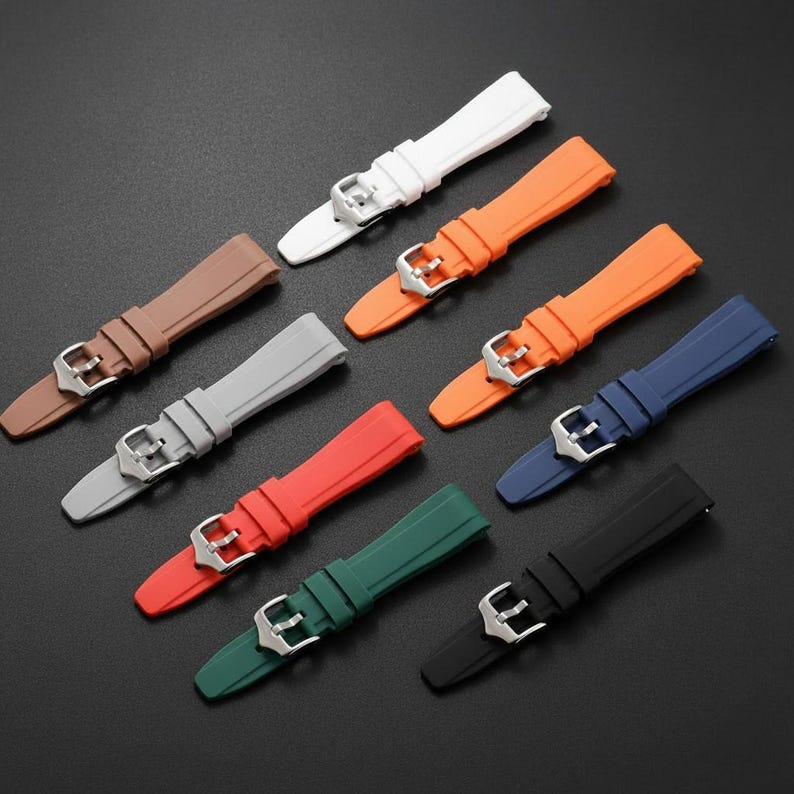 K&ouml;nnte beinhalten: Eine Sammlung von neun Silikon-Uhrenarmb&auml;ndern in verschiedenen Unifarben, darunter Wei&szlig;, Orange, Braun, Grau, Rot, Dunkelgr&uuml;n, Blau und Schwarz. Jedes Armband verf&uuml;gt &uuml;ber eine silberfarbene Metallschnalle und eine passende Schlaufe.