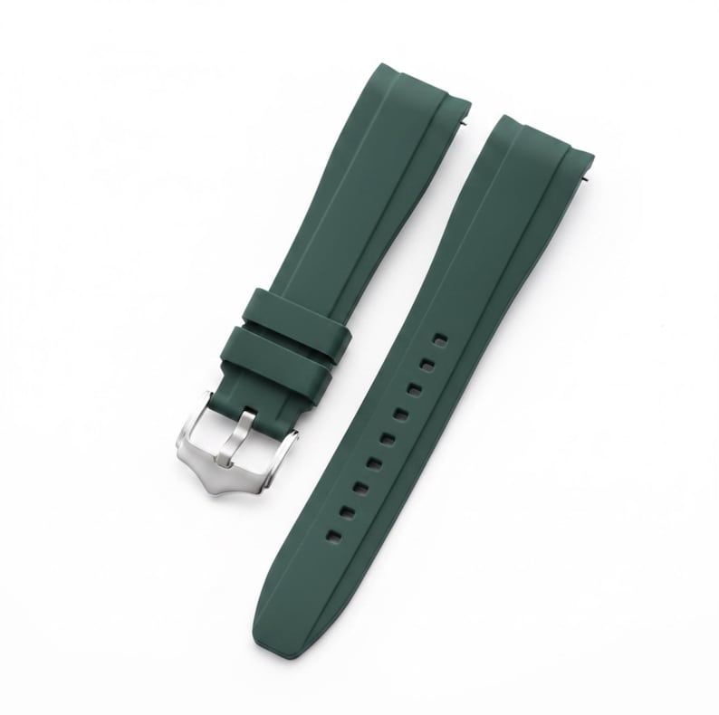 K&ouml;nnte beinhalten: Ein dunkelwaldgr&uuml;nes Uhrenarmband aus Kautschuk, bestehend aus zwei separaten Teilen. Das Armband hat eine glatte, matte Oberfl&auml;che mit einer mittigen, erhabenen Rippe entlang der L&auml;nge jedes Teils. Eine silberfarbene Dornschlie&szlig;e ist befestigt.