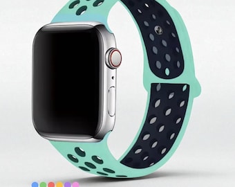 May include: A silver smartwatch with a black screen and a mint green and navy blue band. The band has a perforated design and is made of a flexible material. The watch is displayed on a white background.