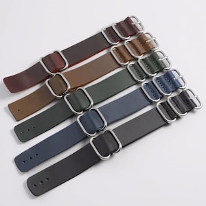 Pode incluir: Uma coleção de pulseiras de relógio de couro em várias cores, incluindo bordô, castanho, verde, azul e preto. Cada pulseira apresenta uma fivela prateada e é projetada para um visual clássico e atemporal. As pulseiras estão dispostas diagonalmente.