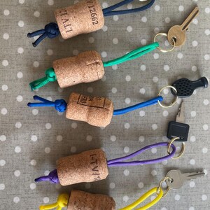 May include: Keyrings made from wine corks with cords in blue, green, blue, purple, and yellow. Each cork has a metal keyring and some have keys attached. The corks have printed text.