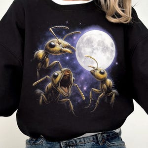May include: Black sweatshirt featuring a graphic of three yellow ants with a full moon and starry background. The ants have detailed features and are in various poses. The word "Black" is printed at the bottom left.