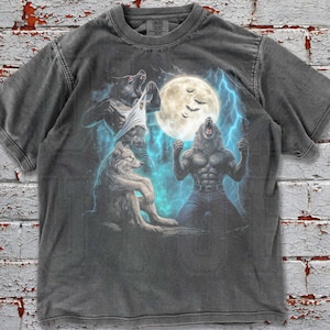 May include: Pepper-colored t-shirt featuring a werewolf graphic under a full moon with lightning. The design includes a wolf and a werewolf transforming. The shirt has a crew neck and short sleeves. The text "OLD FUTURE" is at the bottom right.