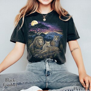 以下が含まれることがあります： 黒色の快適フィットTシャツ。ライオン、ライオン、トラが満月の下、サバンナの風景に描かれた鮮やかなグラフィックが特徴です。シャツの左下には「Black Comfort」の文字がプリントされています。