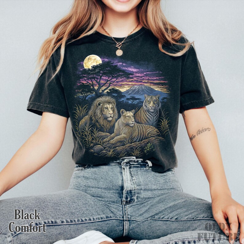 以下が含まれることがあります： 黒色の快適フィットTシャツ。ライオン、ライオン、トラが満月の下、サバンナの風景に描かれた鮮やかなグラフィックが特徴です。シャツの左下には「Black Comfort」の文字がプリントされています。