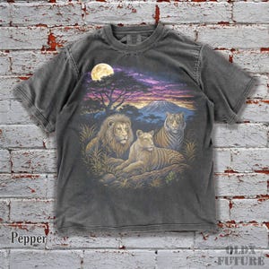 以下が含まれることがあります： 鮮やかな野生生物のシーンが描かれたペッパーカラーのTシャツ。デザインには、満月、木、山のある夕焼け空を背景にしたライオン、ライオン、トラが含まれています。「OLD FUTURE」の文字が見えます。