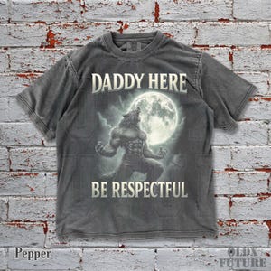May include: Pepper-colored t-shirt featuring a werewolf illustration howling at a full moon. The text "DADDY HERE" is above the image, and "BE RESPECTFUL" is below. The shirt has a vintage, distressed look.