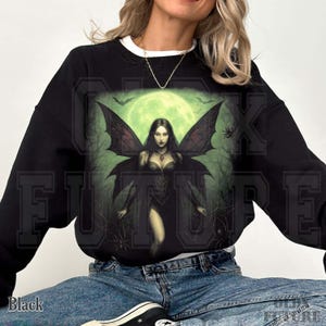May include: Black sweatshirt featuring a gothic fairy design. The graphic shows a dark-haired fairy with large, detailed wings, set against a backdrop of a full moon and trees. The word "FUTURE" is printed on the sweatshirt.