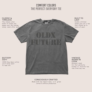 Puede incluir: Una camiseta gris Comfort Colors con el texto "OLDX FUTURE" en una fuente de bloque. La camiseta tiene un cuello redondo cl&aacute;sico y mangas cortas. El texto "COMFORT COLORS THE PERFECT EVERYDAY TEE" est&aacute; en la parte superior.