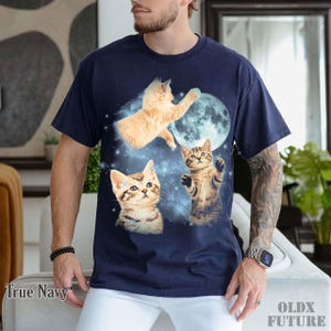 May include: True Navy t-shirt featuring a graphic of three kittens in space with a full moon. The design includes a light orange cat reaching for the moon and two tabby kittens. The text "OLDX FUTURE" is printed on the bottom right.
