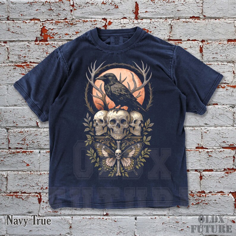May include: Navy blue t-shirt featuring a graphic of a raven perched atop three skulls, with antlers and a butterfly. The design includes an orange moon and foliage. The text "OLDX FUTURE" is visible at the bottom.