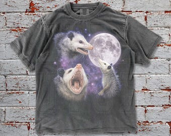 May include: Dark grey t-shirt featuring a graphic of three opossums with the moon and stars. The opossums are in different poses, with one open-mouthed. The shirt has the word "Pepper" at the bottom left.