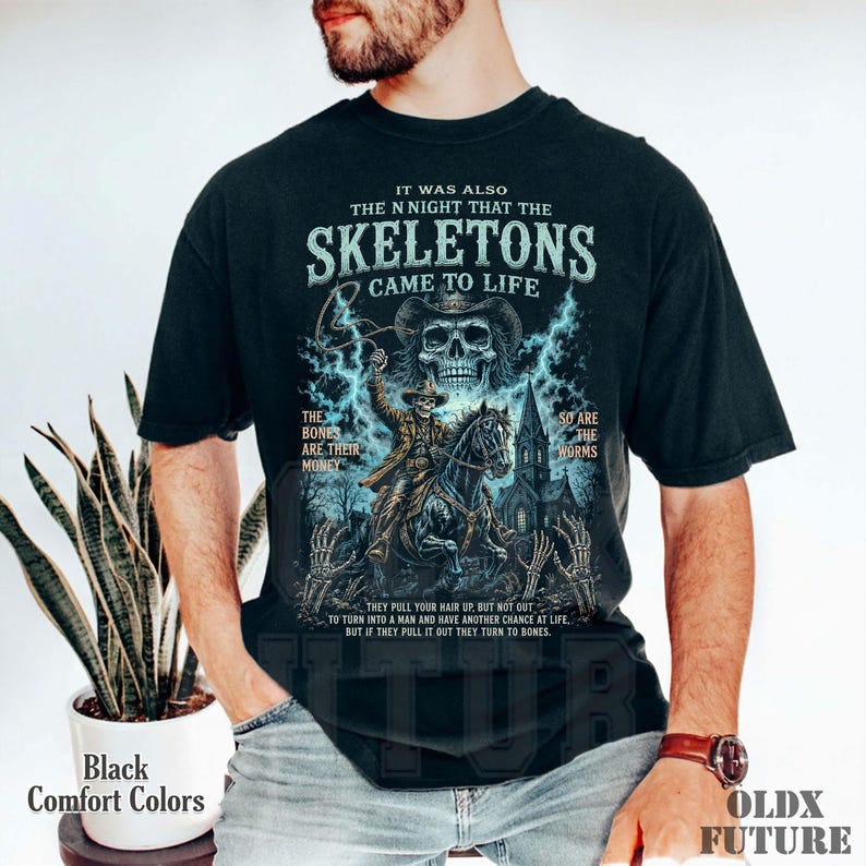 May include: A black t-shirt featuring a graphic print of a skeleton cowboy riding a horse in front of a church. The text reads: IT WAS ALSO THE N NIGHT THAT THE SKELETONS CAME TO LIFE, THE BONES ARE THEIR MONEY, SO ARE THE WORMS.