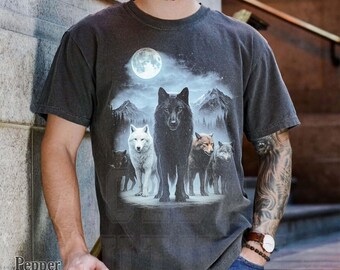 Puede incluir: Camiseta gris oscuro con un diseño de manada de lobos bajo la luna llena. El gráfico incluye un lobo negro, un lobo blanco y otros lobos en un paisaje montañoso. La camiseta tiene un aspecto vintage y desgastado.