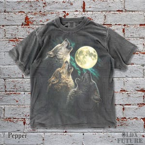 May include: Pepper-colored t-shirt featuring a graphic of three wolves howling at a full moon. The design includes a vibrant moon and aurora borealis effect. The shirt has a classic crew neck and short sleeves.