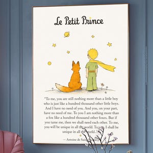 May include: A framed print of "Le Petit Prince" with a fox and a boy, in a room with a pink armchair and ottoman. The print has French text. The room features gold side tables and a window with a view.