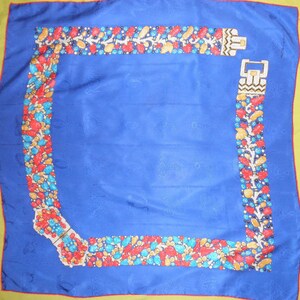 May include: A blue silk scarf with a yellow border. The scarf has a repeating pattern of a jeweled belt with red, yellow, blue, and green stones. The belt is shown in two different positions on the scarf, one at the top and one at the bottom.