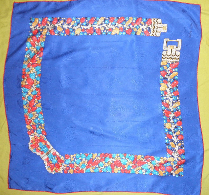 May include: A blue silk scarf with a yellow border. The scarf has a repeating pattern of a jeweled belt with red, yellow, blue, and green stones. The belt is shown in two different positions on the scarf, one at the top and one at the bottom.