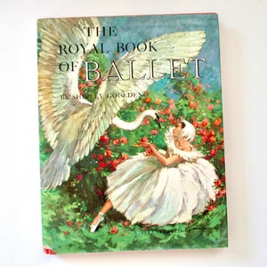 May include: A hardcover book titled The Royal Book of Ballet by Shirley Goulden. The cover features an illustration of a large white swan with spread wings hovering over a person in a white ballet costume amidst a field of red roses.