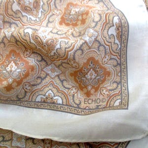 May include: A vintage silk scarf with a paisley pattern in shades of brown, tan, and cream. The scarf has a cream-colored border and the brand name "ECHO" is visible in the corner. The scarf is folded, showing the intricate design.