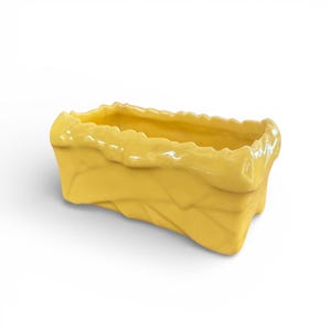 May include: A rectangular, yellow ceramic planter with a textured, woven-like design on the sides. The top edge has a wavy, uneven texture. The planter is a bright, solid yellow color and sits on a white background.