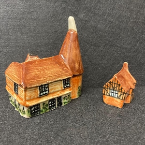 May include: Three miniature ceramic buildings. The largest is a two-story structure with a brown roof and a cylindrical tower. The other two are smaller buildings with brown roofs and detailed facades. The buildings are painted in shades of brown, orange, and green.