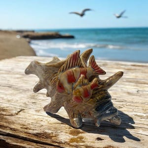 May include: A ceramic seashell with a detailed design of red and white fish. The seashell is brown and has a textured surface.