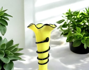 May include: A yellow glass vase with a ruffled top and a black spiral design. The vase is about 10 inches tall.