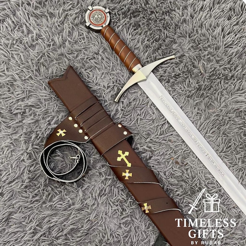 May include: A medieval-style sword with a brown leather-wrapped handle and a silver blade. The sword is displayed with its brown leather sheath, adorned with gold crosses. The sword's hilt features a decorative emblem. The image is set against a gray, textured background.