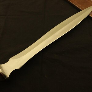 May include: A long, silver-colored blade with a wooden handle and a brass accent. The blade has a sharp point and a wide, flat surface. The handle is dark brown. The sword is approximately 24 inches long.