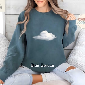May include: Blue Spruce sweatshirt with a white cloud graphic. The long-sleeved crewneck top features the text "Blue Spruce" at the bottom. The sweatshirt is from Comfort Colors.
