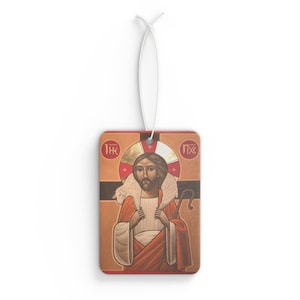 May include: Rectangular air freshener featuring a religious icon of a man with a halo, holding a lamb and a staff. The air freshener has a white string for hanging and is primarily orange, red, and gold in color.