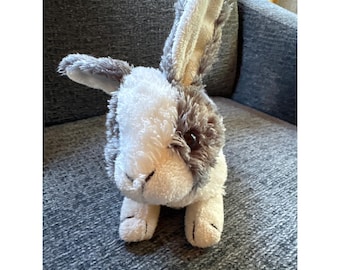 May include: A plush rabbit toy featuring soft, textured fur in shades of white and mottled gray. The stuffed animal has one upright ear and one folded ear, dark brown plastic eyes, and a small stitched nose, with white paws and a fluffy body.