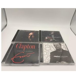 May include: Four Eric Clapton music CDs. The album covers feature images of Clapton and album titles such as "Complete Clapton" and "Clapton Chronicles". The CDs are in clear plastic cases.