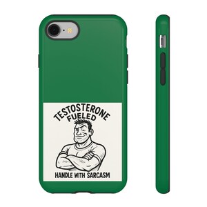 Puede incluir: Una funda de teléfono verde con un rectángulo blanco con un hombre de dibujos animados con los brazos cruzados y el texto "TESTOSTERONE FUELED HANDLE WITH SARCASM". La funda se muestra de frente y de lado.