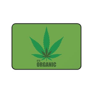 Könnte beinhalten: Ein rechteckiges grünes Mauspad mit schwarzem Rand. Das Design zeigt ein großes grünes Cannabislatt mit einem dunkleren grünen Zentrum. Unter dem Blatt ist der Text "IT'S ORGANIC" in Dunkelgrün gedruckt.