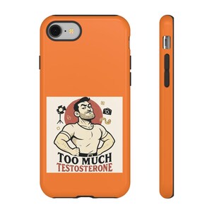 Puede incluir: Funda de teléfono naranja con un gráfico de un hombre musculoso y el texto "TOO MUCH TESTOSTERONE". La funda tiene una lente de cámara negra y botones en el lateral. La funda del teléfono se muestra desde el frente y el lateral.