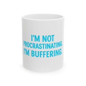 May include: White ceramic mug with the text "I'M NOT PROCRASTINATING. I'M BUFFERING" in light blue. The mug is cylindrical and has a simple, clean design, suitable for coffee, tea, or other beverages.