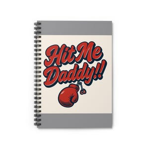 May include: Spiral-bound notebook with a gray cover and the words "Hit Me Daddy!!" in red and blue lettering. A red boxing glove graphic is below the text. The notebook has a cream-colored background.