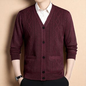 Puede incluir: Un cárdigan burdeos con un patrón de rombos y espiga. El suéter de manga larga tiene cuello en V, dos bolsillos delanteros y botones negros. Se ve una camisa blanca con cuello debajo.