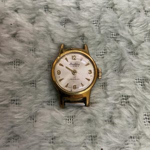May include: A vintage gold-toned Bentima Star wristwatch with a white face. The watch features black numerals, hands, and the text "17 Incabloc Swiss Made". The watch has a small, round face and a gold-colored band.
