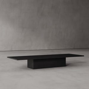 May include: A contemporary black coffee table with a rectangular design. The table features a low, solid base supporting a long, flat tabletop. The dark wood finish gives it a minimalist, modern aesthetic. The table is approximately 200 cm long.